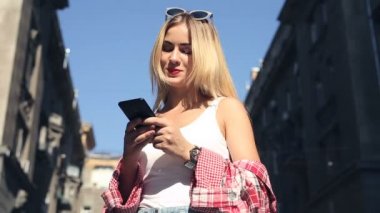 Sokakta ayakta, cep telefonu ile mesaj atıp tutan genç sarışın kadın.