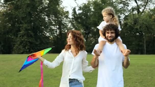 幸せな家族が一緒に公園を散歩します 子供の凧を押しながら父親の肩の上に座っている女の子 — ストック動画