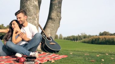 Mutlu çift ekose ağacın yanında oturan. Selfies üstünde smartphone alarak ve having fun.