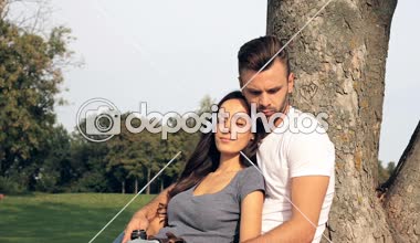 Mutlu çift oturma parkta ağaç yakınındaki ve sarılma.