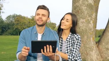 Çift açık havada. Adam Holding tablet ve onlar müzik için lestening birlikte beyaz kulaklık.