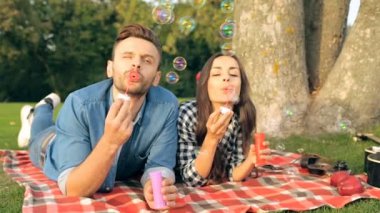 Parkta ağaç yakınındaki ekose yatan bir kaç. Kabarcık üfleyiciler ile eğleniyor. 