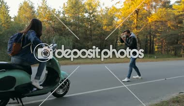 Eğleniyor ve scooter üzerinde oturan genç kadın. Üzerinde anlık görüntü kamera çekim erkek arkadaşı. Onun fotoğraf kartı gösteren ve öpüşme.