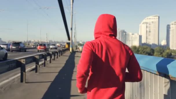 Hombre Con Capucha Roja Corriendo Por Puente Vista Desde Atrás — Vídeos de Stock