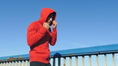 Sporcu kırmızı kapüşonlu eğitim ve boks açık havada köprüde. Slowmotion.