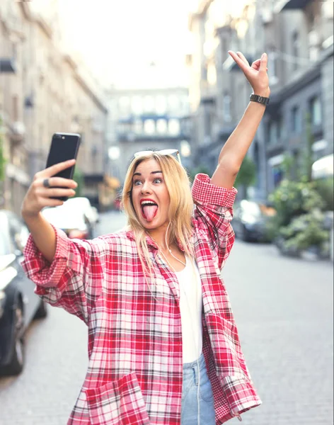 Dalga ve Smartphone'da selfies alarak paece işaret, gösteren komik sarışın kadın.