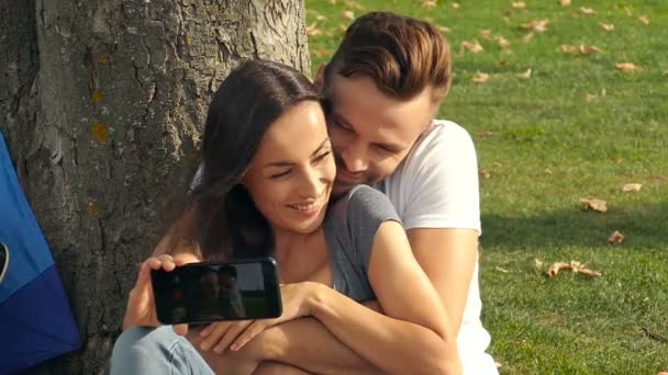 Γελώντας Ζευγάρι Κάθεται Κοντά Στο Δέντρο Και Για Λήψη Selfie — Αρχείο Βίντεο