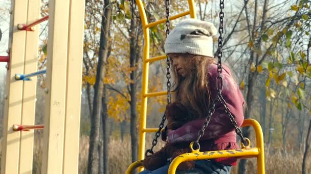 无家可归的女孩与泰迪熊坐在秋千上的操场上 — 图库视频影像