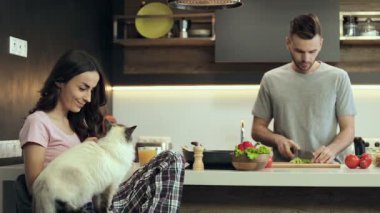 Mutlu genç kadın kedi ve holding smartphone sarılma. Adam salata hazırlık.