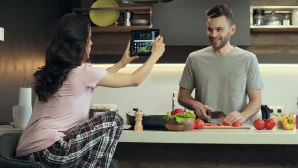 料理のカップル 男は準備サラダとカット野菜 彼の妻 ガール フレンド デジタル タブレットのビデオ撮影と楽しい — ストック動画