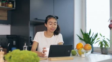 Genç kadın içme kahve, gülümseyerek ve dijital tablet mutfakta kullanma.