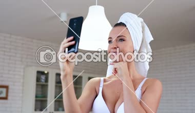 Selfies smartphone üzerinde çekici genç bir kadın portresi. Evde, baş beyaz havlu ile.