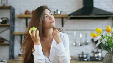 Mutfakta genç bir kadın var. Yeşil elma tutuyor. Bir kenara ve sonra kamera bakıyor.