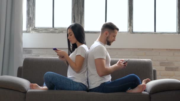 現代の夫婦に戻るソファの上に座って ない感情的な話はありません スマート フォンを持って それを見てします カップルの問題 通信の問題 — ストック動画