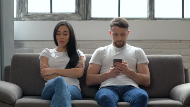 坐在沙发上的夫妇 没有感情 不要说话 愤怒的女子看着男子 而他拿着智能手机看着 一对夫妇的问题 通信问题 — 图库视频影像