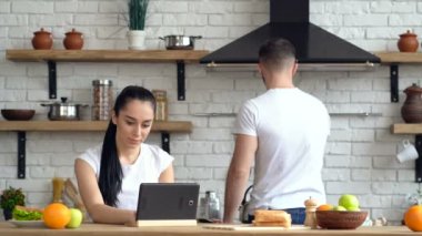 Genç kadın mutfağa laptop bakarak. Genç adam kahve vazgeçiyor.