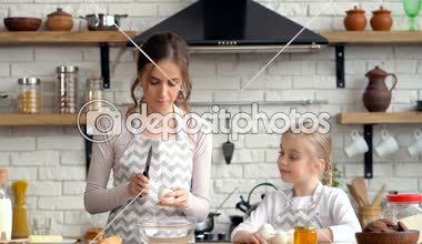 Küçük kızı annesine yardım ediyor. Yumurta vermek. Anne onları plakaya kırıyor.