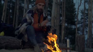 Akşam saatlerinde kamp ateşinin yanında oturan adam..