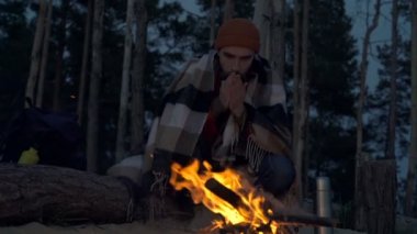 Şenlik ateşinin yanında oturan ve ısınan bir gezgin. Slowmotion.