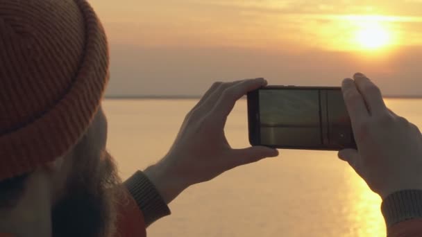 Barba Hombre Sosteniendo Filmando Vídeo Puesta Sol Mar Concéntrate Smartphone — Vídeos de Stock