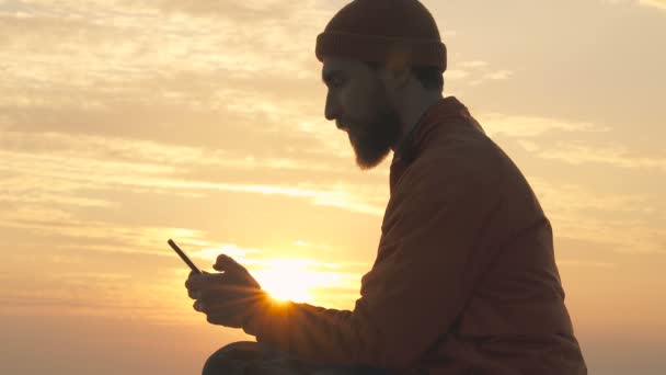 男人坐在沙滩上 手里拿着手机 享受美好的一天 — 图库视频影像