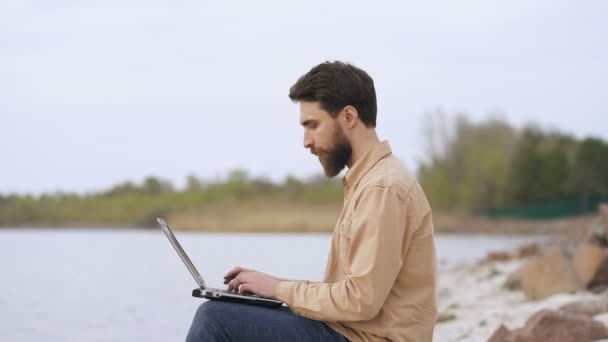 Uśmiechnięty Broda Człowiek Pracujący Laptopem Zewnątrz Pobliżu Morza Lub Jeziora — Wideo stockowe