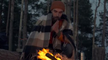 Gezgin adam geceleri kamp ateşinin yanında oturuyor. Ekose giyinmiş, kurtlu eller.
