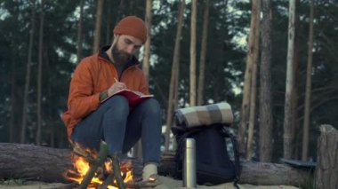 Kamp ateşinin yanında dışarıda dinlenen günlüğü olan bir adam. Günlükte oturma ve yazma.