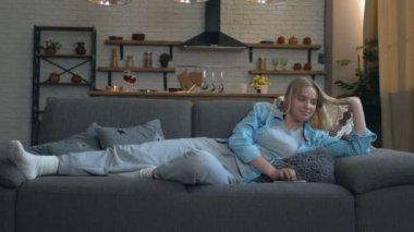 Genç sarışın kadın kanepede uzanıyor ve dinleniyor. Akıllı telefon ve mesaj tutmak. Sonra dinlenmek ve uyumak..