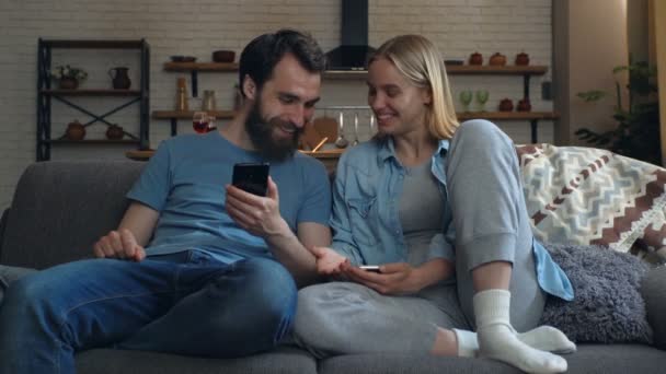Pareja Joven Sentada Sofá Con Smartphones Las Manos Mostrándose Mutuamente — Vídeos de Stock