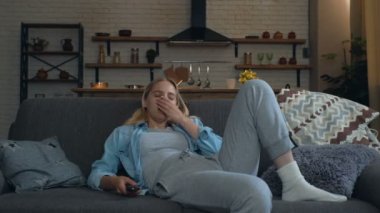 Genç bir kadın evde televizyon seyrediyor, kanepede oturuyor. Uykulu ve yorgun, esniyor. 