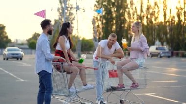 İki genç çift süpermarket arabaları ile otoparkta duruyor. Gülümsüyorlar, konuşuyorlar ve birlikte vakit geçiriyorlar..