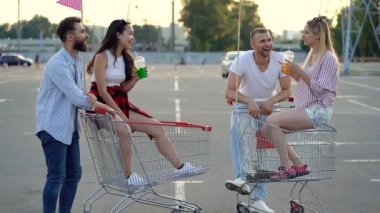 Dört arkadaş otoparkta konuşuyor ve gülümsüyor. Süpermarket arabalarında oturan kızlar. Slowmotion.