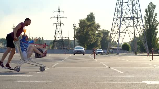 Jong Stel Heeft Plezier Met Supermarkt Trolley Parkeerplaats Rijdend Van — Stockvideo