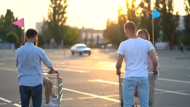 駐車場に立っているスーパーマーケットのカートを持つ4人の友人のグループ 後ろから見る — ストック動画