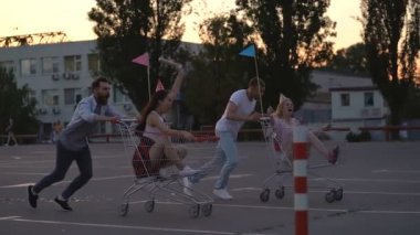 Birlikte eğlenen dört arkadaş. Arabalarla otoparkta koşuyor. Gülmek ve gülümsüyor. Slowmotion. El çekimi.