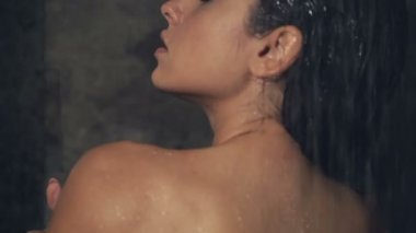 Bayhroom duş altında duran genç esmer kadın closeup görüntüleri. Arkadan görüntüle.