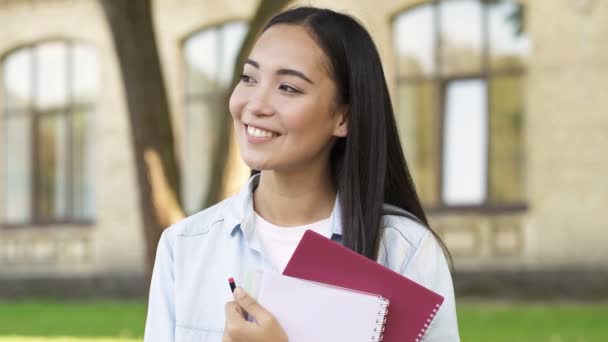 教科書を持っている可愛い笑顔の女子学生の肖像画をクローズアップ 脇を見て カメラを見て — ストック動画