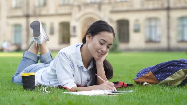 女学生躺在草地上学习 在纸质笔记本上书写 — 图库视频影像