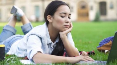 Dizüstü bilgisayarla çalışan yorgun öğrenci kız. Parkta çimenlerin üzerinde yatarken.