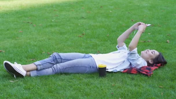 Молодая Азиатка Лежит Зеленой Траве Расслабляет Держит Смартфон Слушает Музыку — стоковое видео