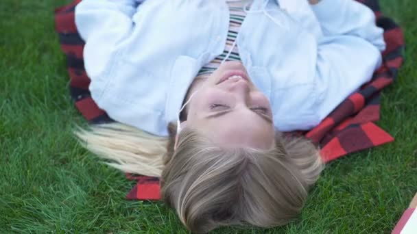 快乐的学生女孩躺在草地上听音乐 顶视图纵向 — 图库视频影像
