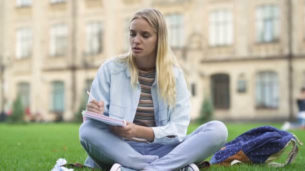 坐在学院附近的草地上的年轻女学生 她很失望 皱着纸 — 图库视频影像