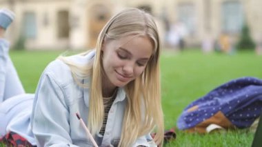 Öğrenci kız dizüstü bilgisayar ile açık havada çalışıyor. Parkta çimenlerin üzerinde yatarken.