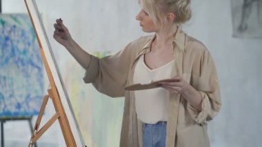 Sanatçı kadın stüdyoda resim çiziyor. Kadına odaklan, sonra da boyama aletleriyle masaya. El yapımı atış. Slowmotion.