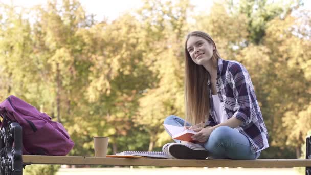 有魅力的女学生坐在学院附近的长椅上 写在练习本上 面带微笑 慢动作 — 图库视频影像