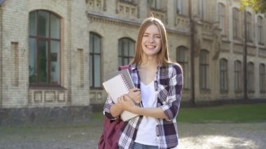Üniversitenin yanında duran güzel bir öğrenci kız. Mutlu, gülümseyen ve neşeli. Kameraya bakıyorum. El yapımı atış. Slowmotion.