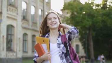 Mutlu ve gülümseyen öğrenci kız üniversite yakınında yürüyüş. Güzel bir yaz günü ve olumlu duygular. Slowmotion.