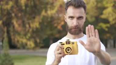 Yakışıklı sakallı adam sarı fotokamera da fotoğraf çekiyor. Kameraya bakmak, gülümseyerek ve işaret ok gösteren.
