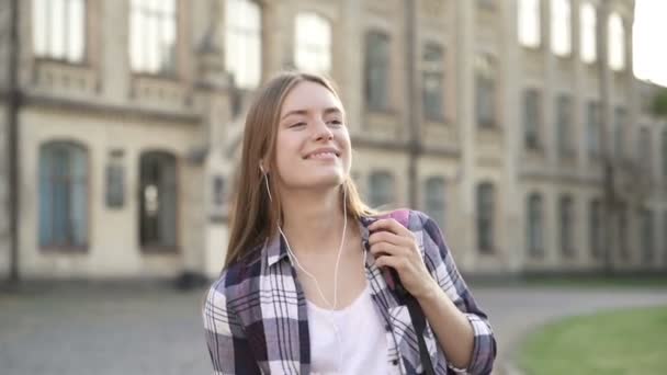 Młoda Uśmiechnięta Kobieta Stoi Zewnątrz Trzymając Smartfon Słuchanie Muzyki Słuchawkach — Wideo stockowe